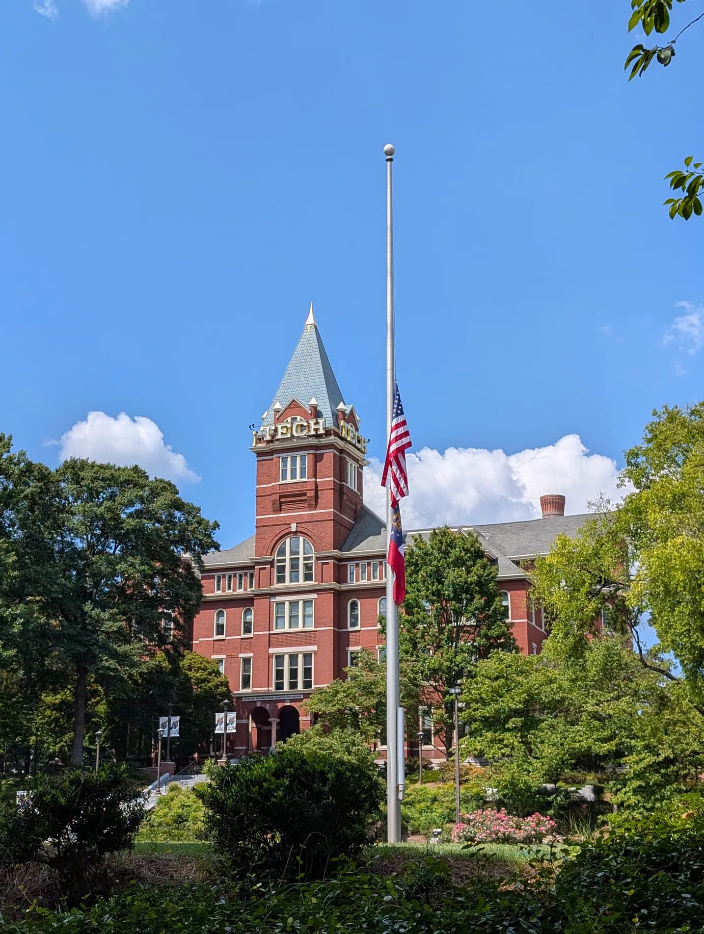 Georgia Tech’s red-brick Tech Tower behind trees and a flagpole, under a blue sky.