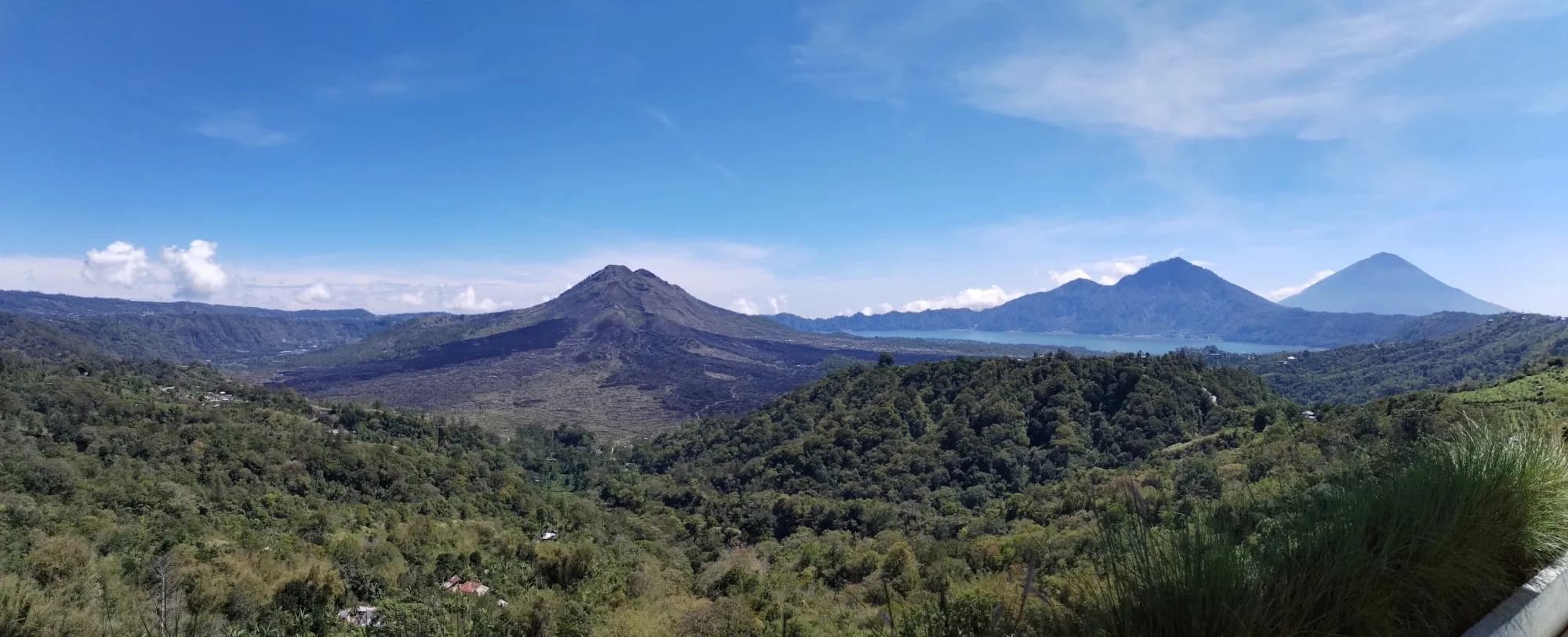 Panorama of Mount Batur and the volcanic ridges beyond, under a blue sky.
