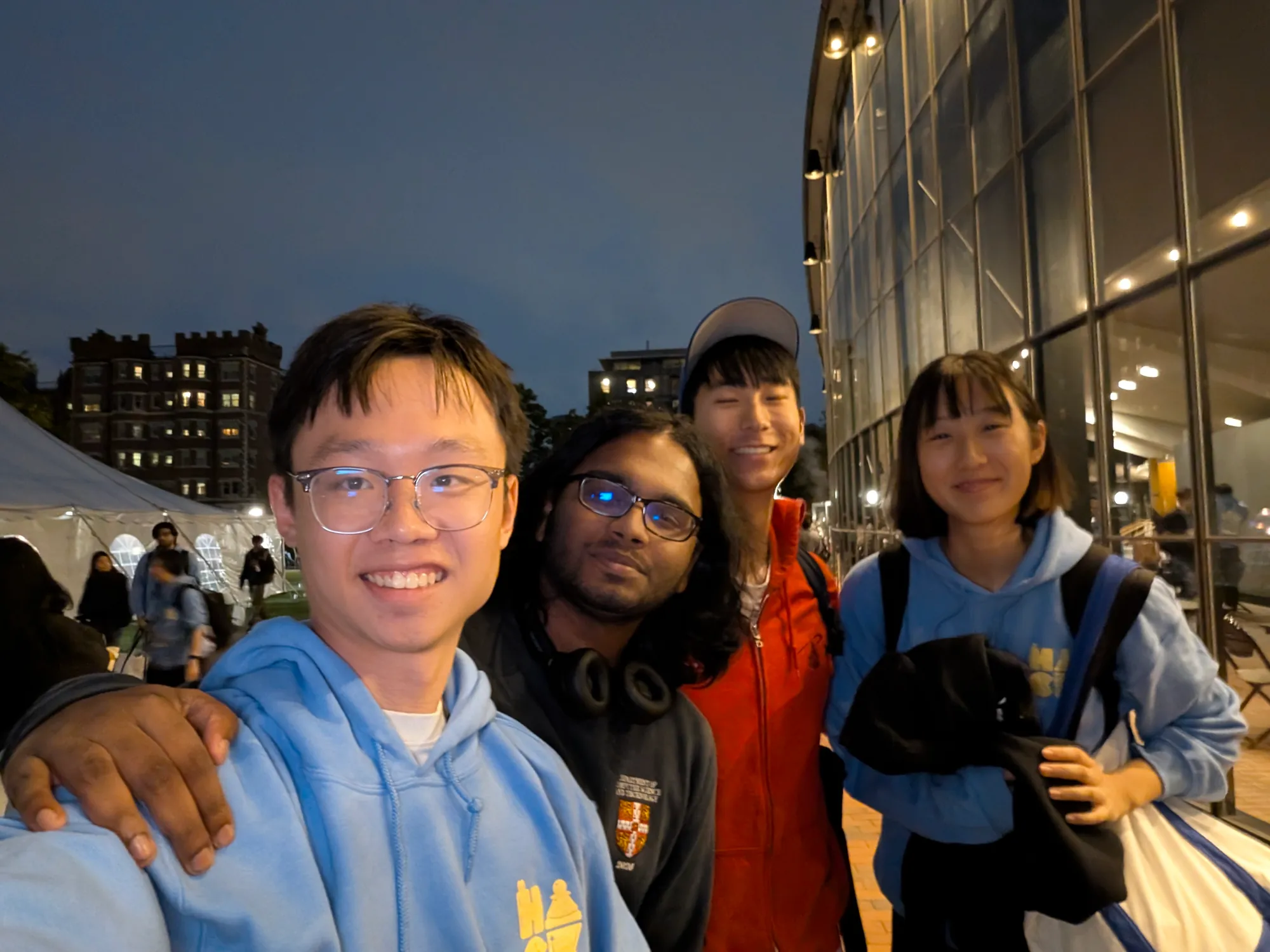 Four friends in a group selfie at night outside a glass building, Boston.