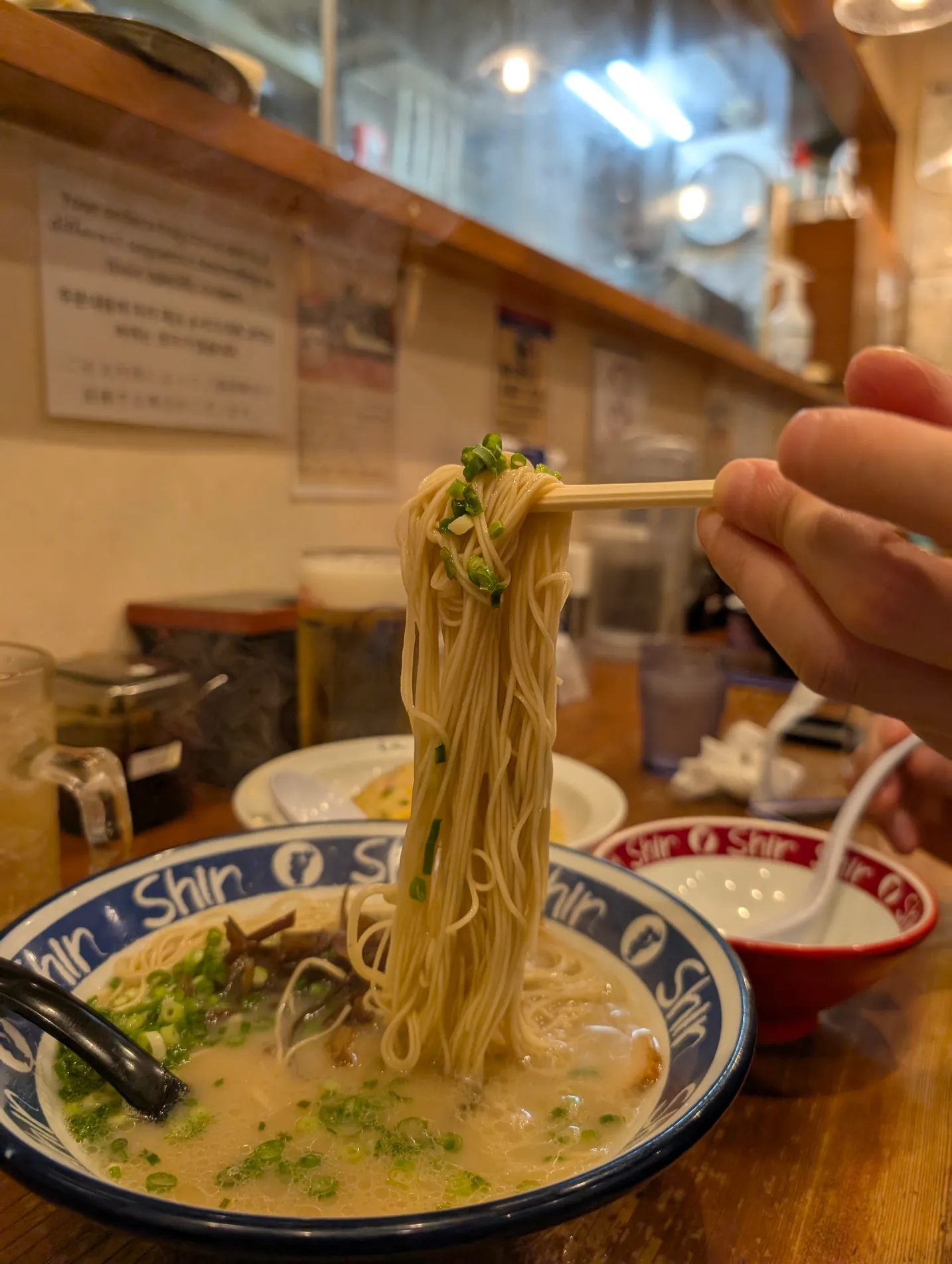 Noodles lifted with chopsticks from a bowl of ramen at a counter, Fukuoka.