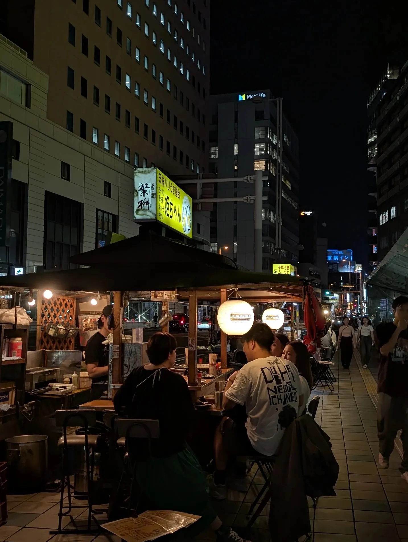 A yatai food stall at night in Fukuoka, customers seated under lanterns.