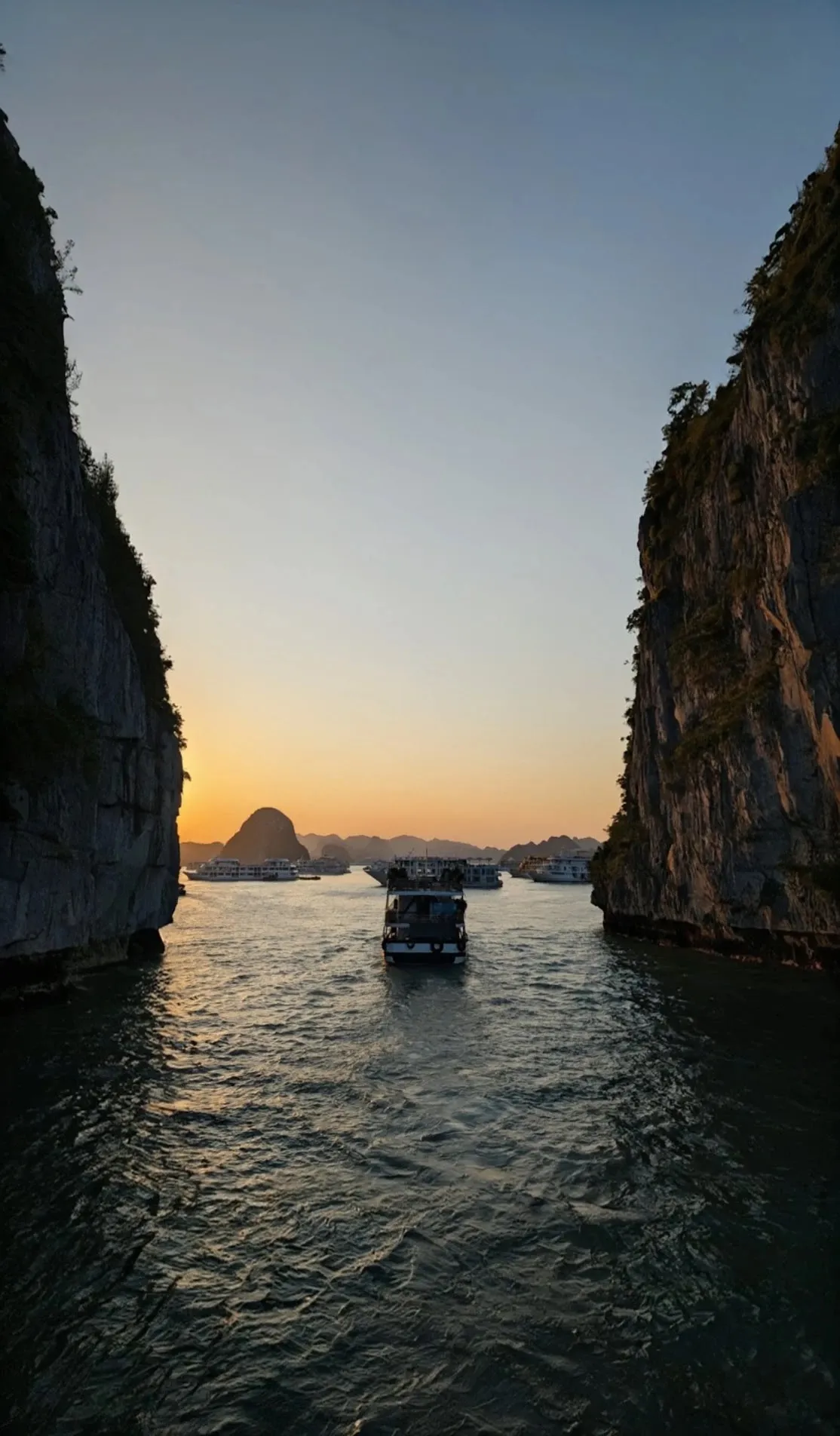 A boat between two limestone cliffs at sunset, Hạ Long Bay.