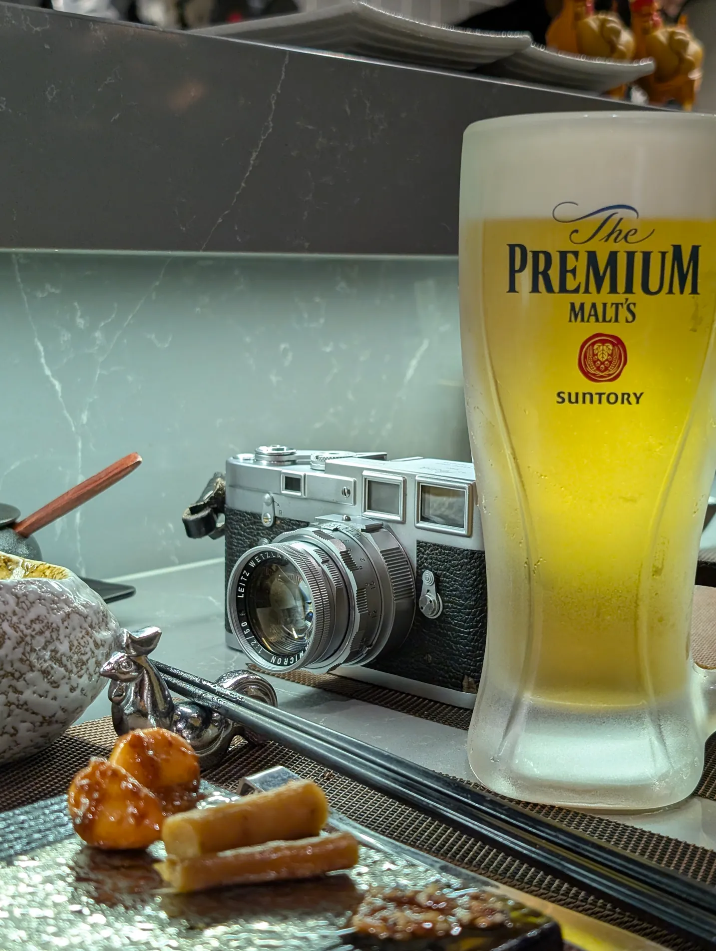 A glass of beer beside a film camera and fried snacks on a bar counter, Hong Kong.
