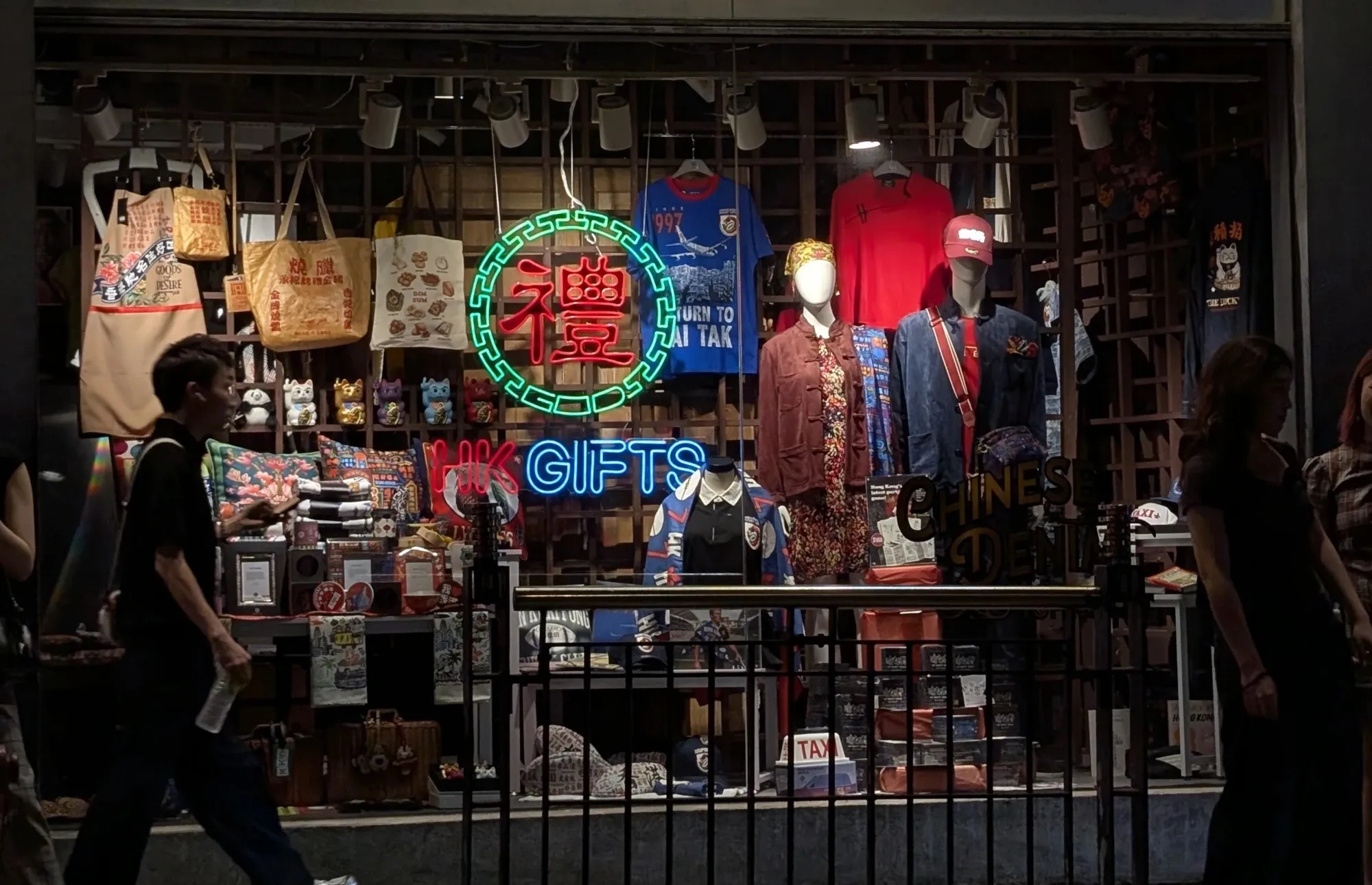 A gift shop window in Hong Kong with a neon sign, mannequins and tote bags.