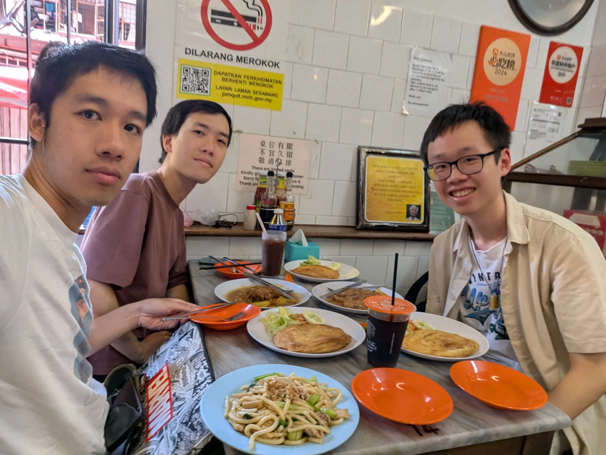 Three friends at a lunch table crowded with plates of noodles and rice, Kuala Lumpur.