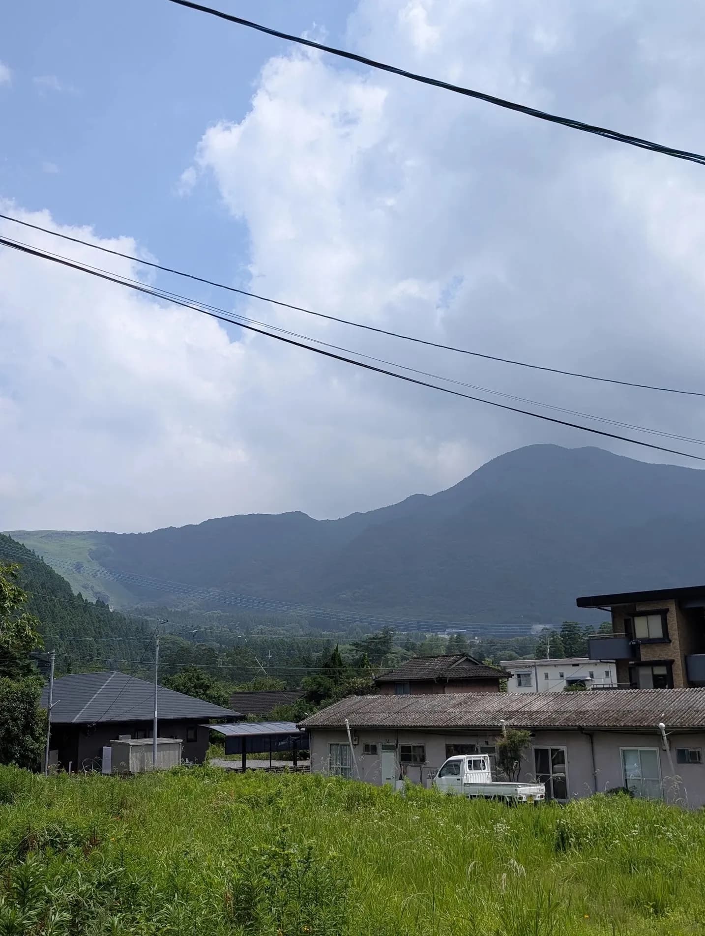 Power lines over low houses and green hills in the Kyushu countryside.