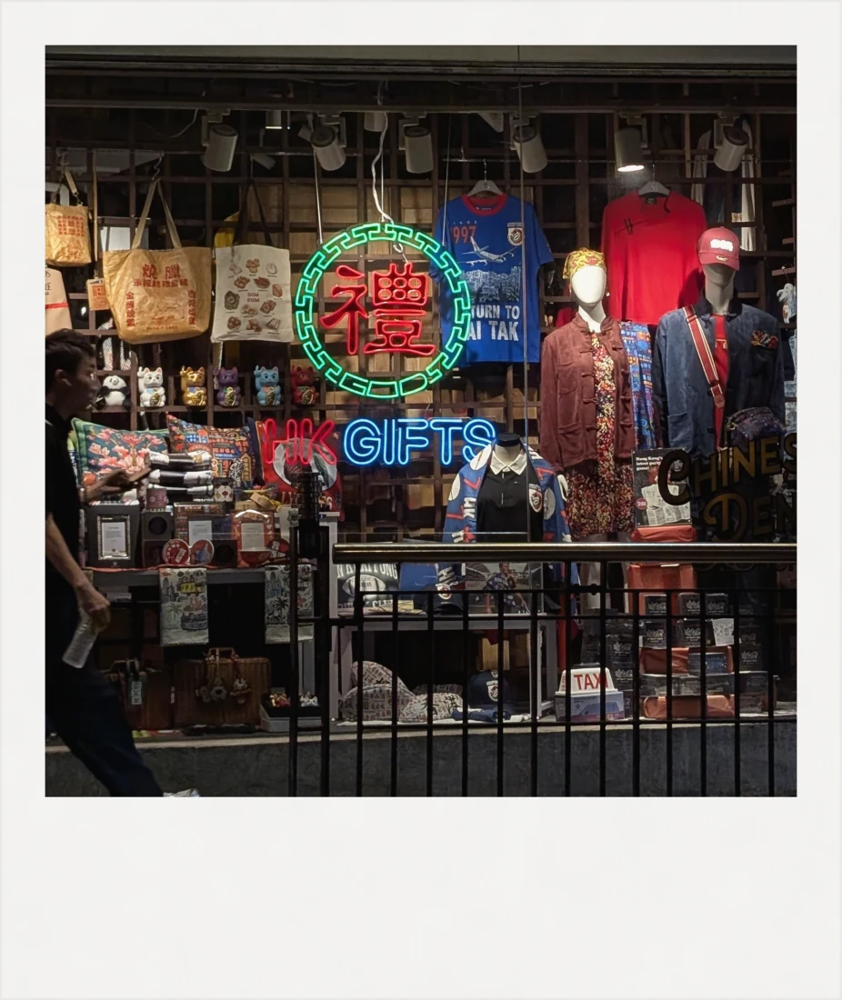 A gift shop window in Hong Kong with a neon sign, mannequins and tote bags.
