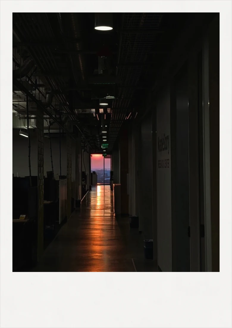 A long dark corridor ending in a window lit orange by the sunset.